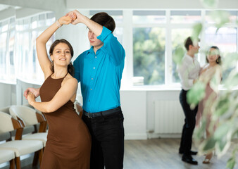 Graceful young girl enjoying impassioned merengue with male partner in latin dance class in studio....