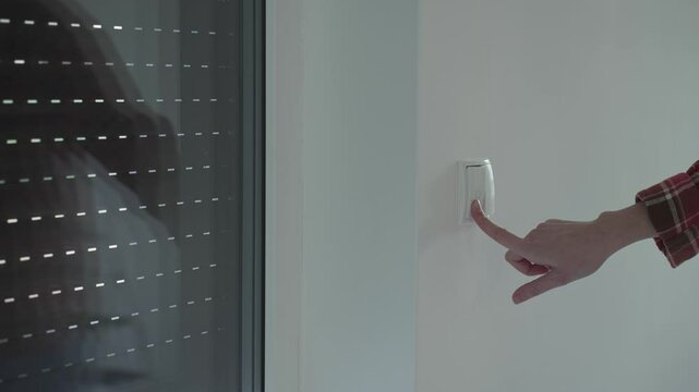 Hand pressing a wall switch to control electric window blinds in a modern home. Smart home automation, convenience, and energy efficiency