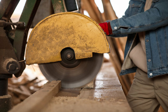 Male carpenter using sawing machine at sawmill, closeup