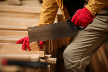 Male carpenter sawing wooden plank at sawmill, closeup