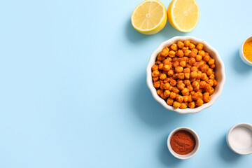 Bowl of tasty fried chickpeas with lemon and spices on blue background