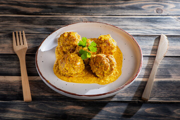 Plate with juicy meatballs in almond sauce on a rustic wooden table, close-up.