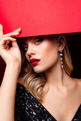 Elegant blonde woman in a glamorous outfit holding a red backdrop banner, showcasing timeless...