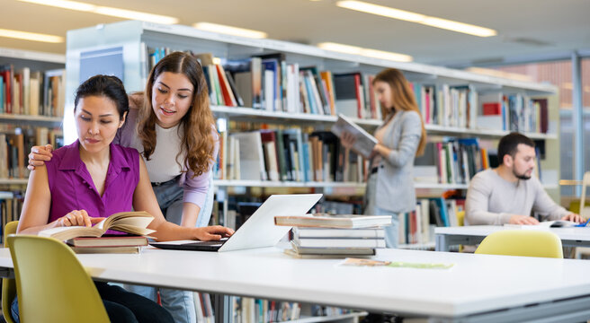 Caring woman helping friend to prepare for exams in public library