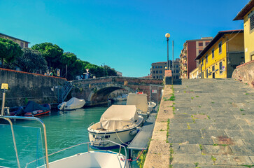 A picturesque city canal on a sunny day. Moored boats line the waterway next to a stone quay and...