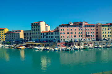 Colorful historic buildings line a picturesque city harbor filled with moored boats. The calm...