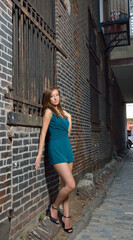 Beautiful young Caucasian female model poses in cobblestoned alley wearing a blue-green romper
