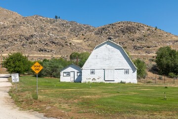 Rural scene of a white barn and outbuilding, with a dead end sign on a primitive road. The location...