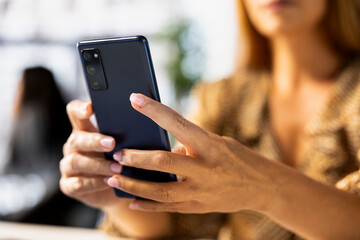 Business manager browses her smartphone researching new strategies and project planning tools. Using mobile device as tool for decision making and collaboration in the workplace. Close up.