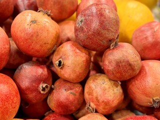 Lots of ripe red pomegranates on a market counter for sale on sale in vegetable stand display at supermarket show organic food, vegetarian food, healthy food. Close-up