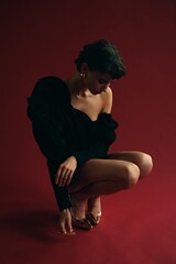 Elegant pose of a woman in black outfit against red backdrop during an artistic photoshoot