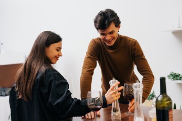 A couple smiles and shares a light moment while pouring wine at a cozy table
