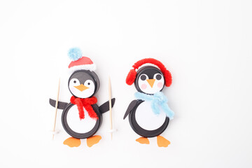 Two adorable penguin crafts made from bottle caps, featuring winter accessories like earmuffs, scarves, and Santa hats. Perfect for Christmas decorations, kids crafts, and eco-friendly DIY projects