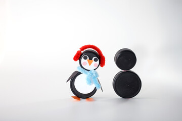 DIY penguin and snowman crafts made from plastic bottle caps with pipe cleaner accessories on a white background. Studio shot. Winter and Christmas craft idea for design and print,
