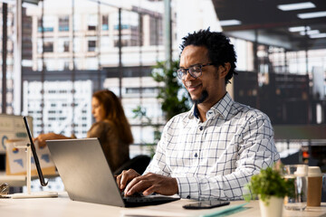 African american general manager reviews business forecasts and plans on his laptop at office desk,...