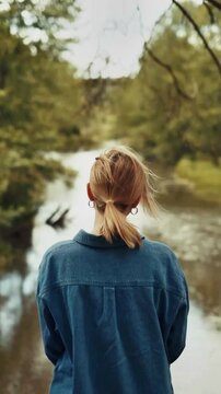A Lady Standing Near a River Surrounded by Green Trees on a Daytime Natural Landscape.