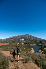 Father and daughter hiking on mountain trail near scenic lake under clear blue sky, La Concepcion reservoir in Marbella