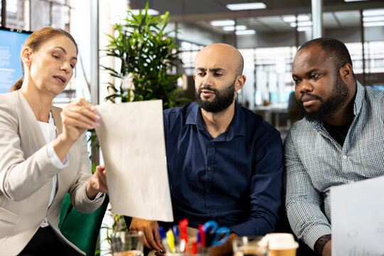 Multiracial team of accountants looking over revenue figures on documents in office. Multiethnic workers in office comparing company statistical numbers, working hard to finish job before deadline