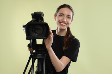 Happy woman with professional video camera on pale olive background