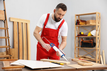 Worker with caulking gun glueing wooden plank indoors