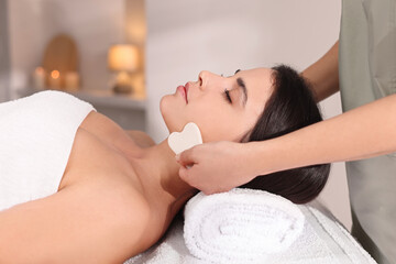 Young woman receiving facial massage with gua sha tool in spa salon