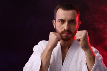 Karate fighter in color lights and smoke against black background. Space for text