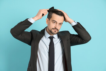 Handsome man stylish his hair with comb on light blue background