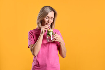 Woman drinking tasty cucumber water on orange background, space for text. Refreshing drink