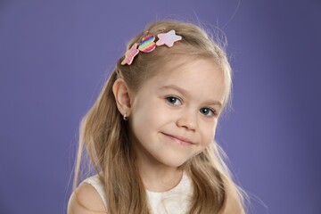 Cute little girl with beautiful hair clips on violet background