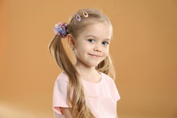 Cute little girl wearing beautiful hair accessories on light brown background