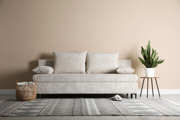 Comfortable sofa with pillows, houseplant and basket near beige wall