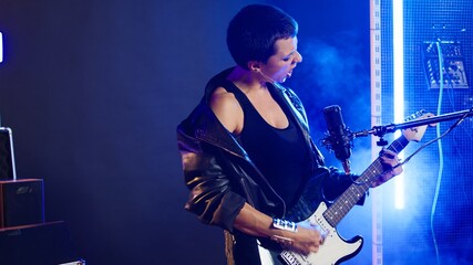 Obraz premium Rock star woman in a leather jacket playing a heavy metal set, shredding her electric guitar with energy. Bold rebellious musician with a grunge style defines her iconic live performance. Camera A.