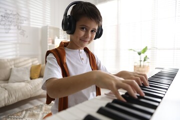 Cute boy in headphones playing synthesizer at home © New Africa