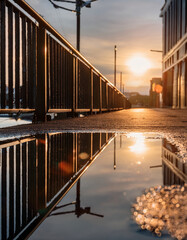 A beautiful sunset reflects in a puddle on an urban sidewalk, creating a stunning mirror effect.