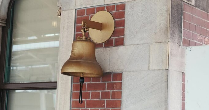A bronze bell is seen on the exterior of Istanbul's historic Sirkeci Train Station. The bell hangs in front of the station's characteristic stone and brick wall.