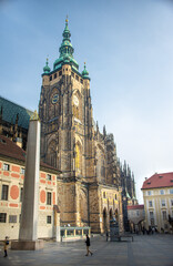 The magnificent, Gothic St. Vitus Cathedral stands tall under a bright blue sky, featuring intricate architectural details and green-tipped spires on a summer day in Prague, Czech Republic.