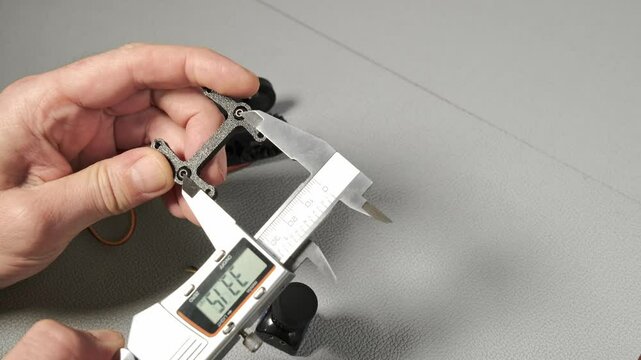 An engineer works with a digital caliper to measure a small robotic servo component with gears and wiring. Taking size, wide, length The precise measurement is shown on the LCD screen of the tool.