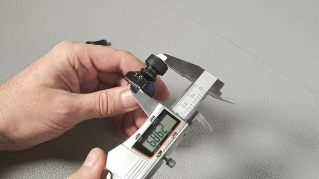 An engineer works with a digital caliper to measure a small robotic servo component with gears and wiring. Taking size, wide, length The precise measurement is shown on the LCD screen of the tool.