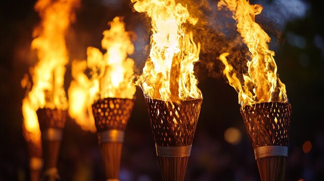 Dramatic close-up of burning tiki torches in the dark, with bright orange flames dancing against black background, creating a tropical ambiance for outdoor evening events.