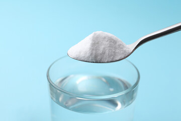 Adding baking soda to glass of water on light blue background, closeup