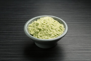 Wasabi powder in bowl on black textured table, closeup