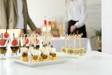 Many different tasty canapes on white table. People enjoying buffet meals indoors, closeup