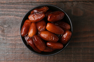 Tasty dried dates in bowl on wooden table, top view