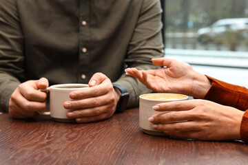 Colleagues having coffee break at wooden table in cafe, closeup
