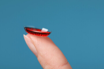 Woman with red color contact lens on light blue background, closeup