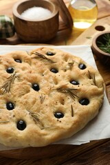 Delicious focaccia bread with olives, rosemary and salt on wooden table, closeup