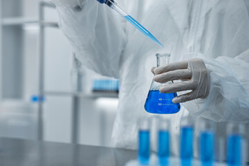 Scientist dripping blue sample into flask in laboratory, closeup