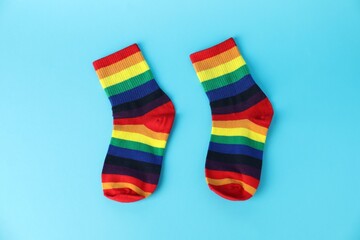 Pair of socks in LGBT colors on light blue background, flat lay