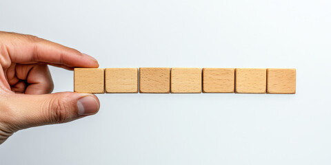 A hand places a blank wooden tile in a row of others on a white surface. Use this for word games, creativity, or concepts requiring text on websites/blogs.