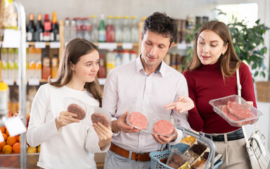 Couple adult man and young woman with teenage daughter buy hamburger patty or beef entrecote in grocery store